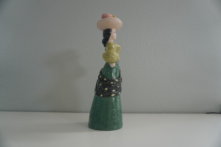 A figurine of a woman carrying fruit on her head, side view.