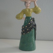 A figurine of a woman carrying fruit on her head.