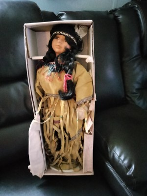 A doll in a box, dressed in a Native American style.