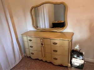 A cream colored dresser with mirror.