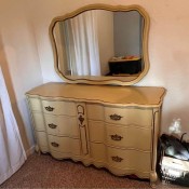 A cream colored dresser with mirror.